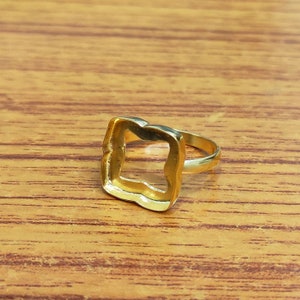 Könnte beinhalten: Ein goldfarbener Ring mit einem quadratischen, offenen Zentrum. Der Ring ist aus Metall und hat eine glatte Oberfläche.