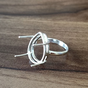May include: A silver ring setting with a pear-shaped design. The ring features a band and a detailed setting to hold a gemstone. The setting has four prongs to secure the stone. The ring is shown on a wooden surface.