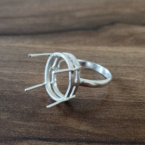 May include: Silver ring setting with a double oval bezel and prongs. The setting is designed to hold a gemstone or other material.