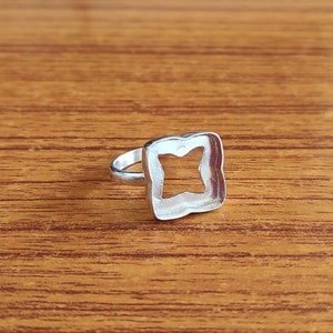 May include: Silver ring with a square-shaped setting. The setting has a cutout in the shape of a four-pointed star.