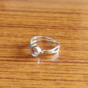 May include: A silver ring with a round bezel setting. The ring is made of two bands that are twisted together.