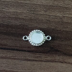 Può includere: Pendente rotondo argentato con una montatura a bezel e due anelli di salto. Il pendente ha un bordo perlato.