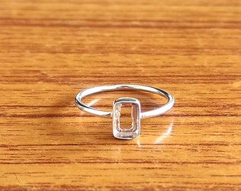 May include: A silver ring with a rectangular bezel setting. The ring is designed to hold a stone or other embellishment.