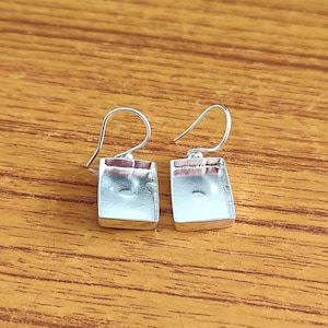 Puede incluir: Un par de pendientes de plata con forma cuadrada. Los pendientes tienen un diseño sencillo y son perfectos para el uso diario.