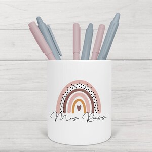 May include: White ceramic pencil holder with a rainbow design and black polka dots. The rainbow is in shades of pink, brown, orange, and yellow. The text "Mrs. Russ" is written below the rainbow.