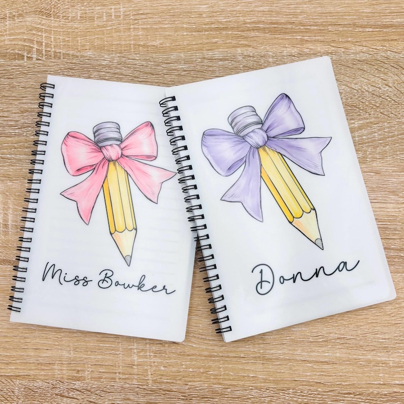 May include: Two white spiral notebooks with personalized names, "Miss Bowker" and "Donna". Each notebook features a yellow pencil with a pink and purple bow, respectively.