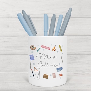 May include: White ceramic pencil holder with a blue and white design featuring school supplies and the text "Mrs. Collins".