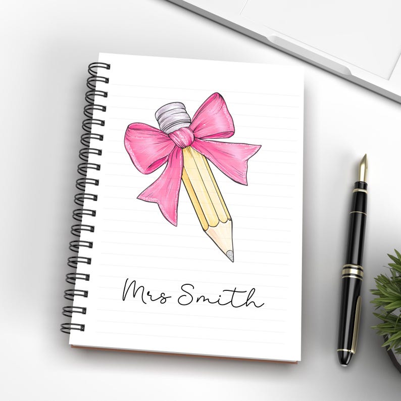 May include: A spiral bound notebook with a pink bow tied around a yellow pencil. The notebook has the name "Mrs. Smith" written on the front.