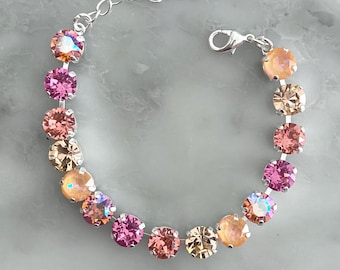 May include: A silver bracelet featuring a series of round, colorful gemstones in shades of pink, peach, and gold. The bracelet has a delicate chain and clasp closure, perfect for adding a touch of sparkle to any outfit.