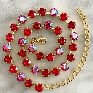 Könnte beinhalten: Eine goldfarbene Kettenhalskette mit einer Reihe runder, facettierter roter Kristalle und irisierender rot-rosa Kristalle, die in Metallfassungen eingefasst sind. Die Halskette ist spiralförmig angeordnet und verfügt über einen Karabinerverschluss.