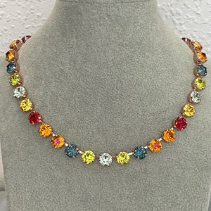 May include: A necklace featuring a series of round, multi-coloured faceted stones set in a rose gold-toned metal chain. The stones display a vibrant spectrum of colours including red, orange, yellow, lime green, and blue, arranged in a repeating pattern.