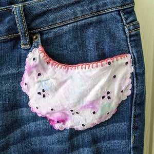 Könnte beinhalten: Eine blaue Jeanshose mit einem rosa und weißen bestickten Taschentuch, das in die vordere Tasche eingenäht ist.