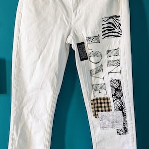 Puede incluir: Vaqueros blancos de denim con parches cosidos en la pierna derecha. Los parches incluyen un estampado de cebra, cuadros, paisley y un dibujo de la palabra "LOVE" con las palabras "FOREVER YOUNG" escritas en un pequeño parche.