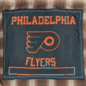 May include: A black and orange patch with the text "PHILADELPHIA FLYERS" and the team's logo, a winged 'P', on a brown plaid background.