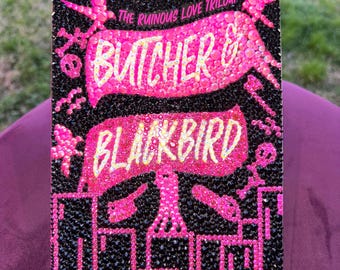 May include: A book cover with a black background covered in small, sparkling black gems. The title "Butcher & Blackbird" is in bright pink, with the author's name, Brynne Weaver, below. The book is part of "The Ruinous Love Trilogy."