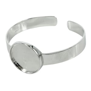 May include: Silver bangle bracelet with a round, blank, glass cabochon setting. The bracelet is open and has a smooth, polished finish.