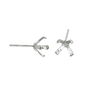 May include: A pair of silver earring settings with four prongs each. The settings are designed to hold a gemstone or other embellishment.