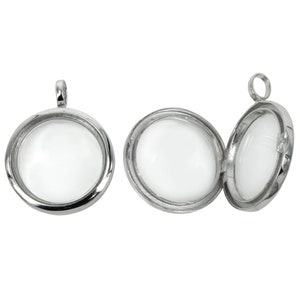 Puede incluir: Medallón colgante de plata con un inserto redondo de vidrio transparente. El medallón está abierto para revelar el interior.
