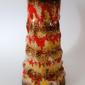 Könnte beinhalten: Eine hohe, braune Keramikvase mit strukturierter Oberfläche. Die Vase ist mit roter, gelber und weißer Glasur verziert, was einen marmorierten Effekt erzeugt.