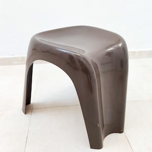 May include: A brown plastic stool with a curved seat and legs. The stool has a glossy finish and is designed with a modern aesthetic. The stool is suitable for indoor or outdoor use.