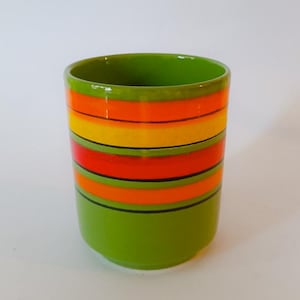 Pode incluir: Uma caneca de cerâmica verde com listras laranja, amarelas e pretas.