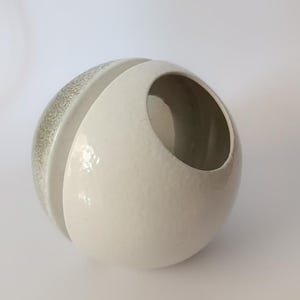 May include: A white ceramic planter with a textured surface and a green glazed rim. The planter is shaped like a sphere with a hole in the side.