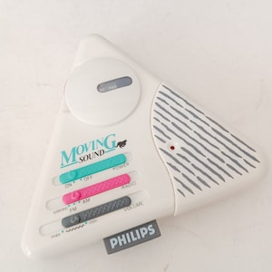 Può includere: Una radio bianca a forma triangolare con un logo di pantera nera e il testo "Moving Sound". La radio ha un quadrante con il testo "92 600", e pulsanti per "On", "Off", "Power", "Radio", "Stereo", "AM", "FM", "Volume", e "Max" e "Min". La radio ha anche un logo Philips.