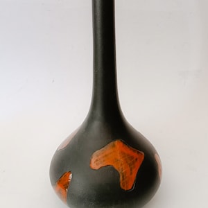 Può includere: Un vaso in ceramica nera con collo lungo e base arrotondata. Il vaso è decorato con forme geometriche arancioni.