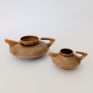 May include: A set of two brown ceramic teapots with a textured surface. The larger teapot has a lid and a handle. The smaller teapot has a handle.