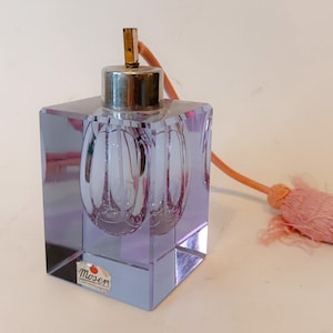 Könnte beinhalten: Ein quadratischer, lavendelfarbener Parfümflakon mit silberfarbenem Deckel und goldfarbenem Zerstäuber. Die Flasche hat ein Innendesign und eine rosa Quaste. Das Etikett lautet "Moser Czechoslovakia".