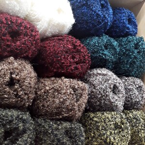 Puede incluir: Una pila de ovillos de lana de colores en varios tonos de rojo, azul, verde, marr&oacute;n y blanco. La lana es esponjosa y texturizada, perfecta para tejer o hacer ganchillo.