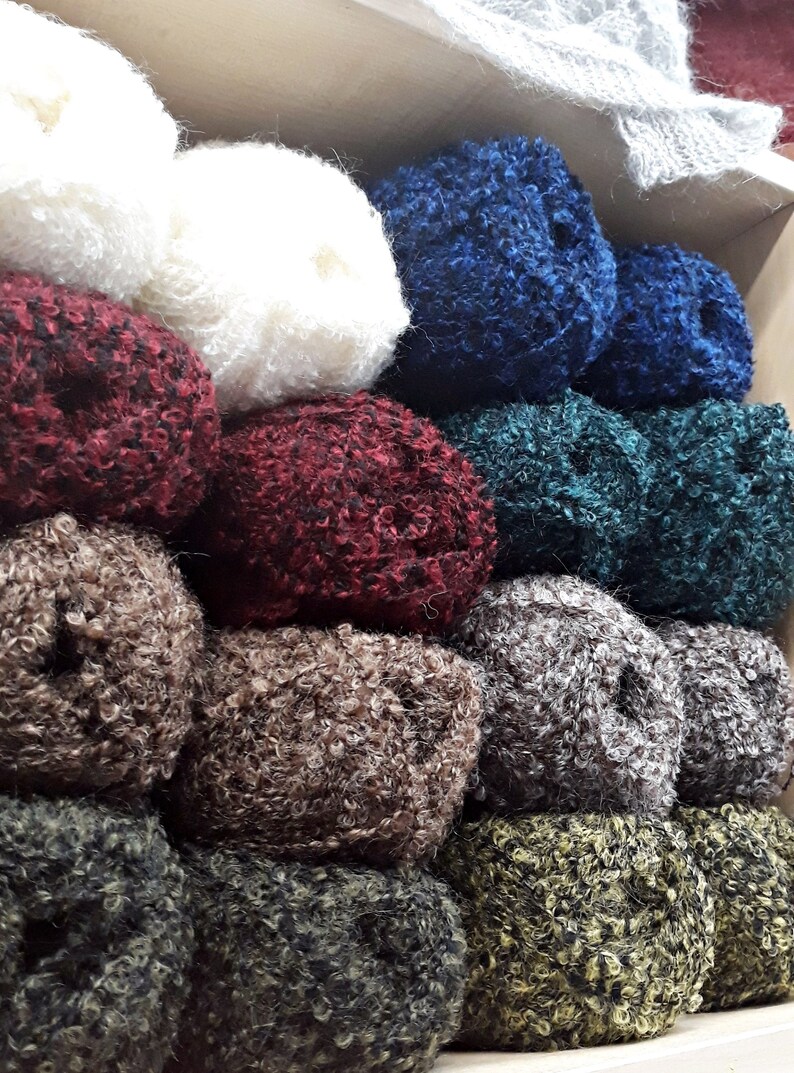 Puede incluir: Una pila de ovillos de lana de colores en varios tonos de rojo, azul, verde, marr&oacute;n y blanco. La lana es esponjosa y texturizada, perfecta para tejer o hacer ganchillo.