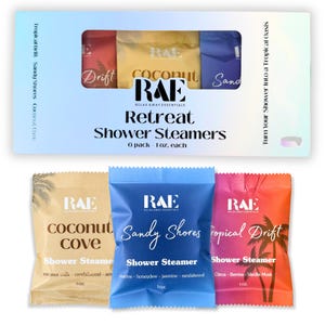 May include: A box set of RAE Retreat Shower Steamers. The box contains six 1 oz. steamers in various colors: yellow, blue, and red. Individual packets are labeled "Coconut Cove", "Sandy Shores", and "Tropical Drift". The packaging features palm tree graphics.
