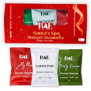 May include: A red rectangular box labeled Santa's Spa Shower Steamers containing six 1 oz shower steamers. Below the box are three individual packets: a red Jolly Bliss packet, a white North Pole packet, and a green Frosty Escape packet.