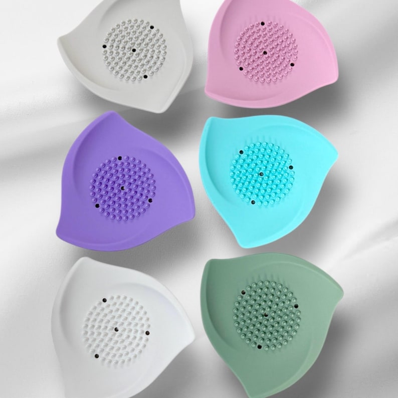 May include: A collection of six colorful silicone face scrubbers. Each scrubber is leaf-shaped with a textured center for exfoliation. Colors include white, pink, purple, teal, and green.