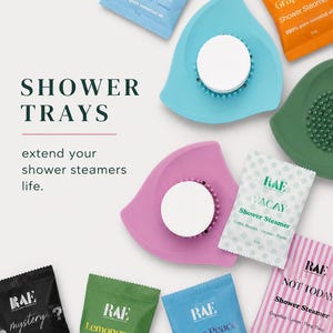 May include: An overhead shot displays shower trays and shower steamers. The trays are in various colors, including blue, green, and pink. The shower steamers come in different scents, such as "Inner Peace" and "Orange Grapefruit."