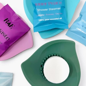 May include: An overhead shot of shower steamers and trays. The trays are in shades of pink, teal, and green. The shower steamers are in small packets with the text "Inner Peace" and "100% pure essential oil".