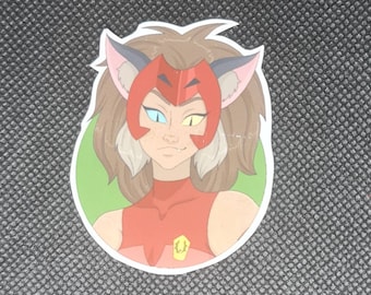 May include: A die-cut sticker featuring a cartoon character with brown hair, wearing a red headpiece with pointed ears and a red top with a yellow emblem. The character has heterochromia, with one blue eye and one yellow eye, set against a green circle.