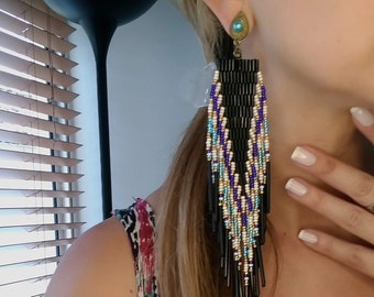 May include: A pair of long, black beaded earrings with blue, white, and gold accents. The earrings are dangling and have a fringe-like design.
