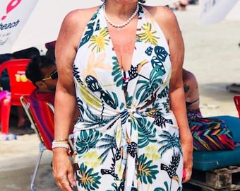 May include: A woman wearing a green visor, sunglasses, and a white halter top with a tropical print. The top has a knotted front and features toucans and palm trees. She is standing in front of a beach umbrella with the text "floripabeach" printed on it.