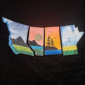 May include: Four embroidered felt patches depicting different landscapes of Canada. The patches are shaped like the provinces of British Columbia, Alberta, Saskatchewan, and Manitoba. Each patch features a unique landscape, including mountains, trees, and water.