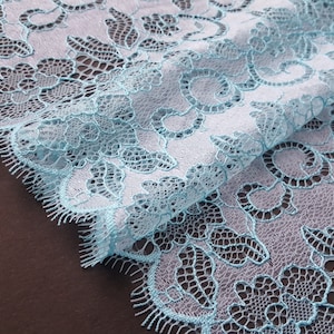 May include: Light blue lace fabric with a delicate floral pattern. The lace has a scalloped edge.