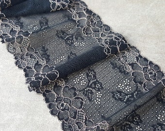 Könnte beinhalten: Nahaufnahme eines schwarzen Spitzenstoffs mit floralem Design. Die Spitze hat ein zartes Muster mit einem gewellten Rand und einem kontrastierenden Metallic-Faden. Der Stoff ist gefaltet und zeigt seine Textur und Details. Ideal für Näh- und Bastelprojekte.