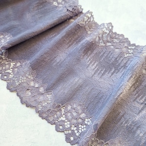 May include: A close-up of a grey lace trim with a delicate floral pattern. The lace is soft and flowing, and it would be perfect for adding a touch of elegance to any project.