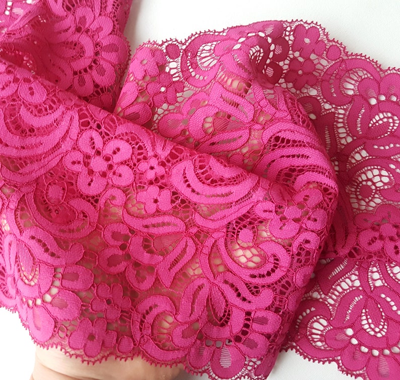 May include: Pink lace trim with a delicate floral pattern. The lace has a scalloped edge.
