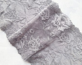 Puede incluir: Primer plano de un trozo de tela de encaje gris. El encaje presenta un patrón floral con diseños detallados de rosas y hojas. La tela está doblada, mostrando la intrincada textura y el delicado calado. Ideal para proyectos de costura y manualidades.