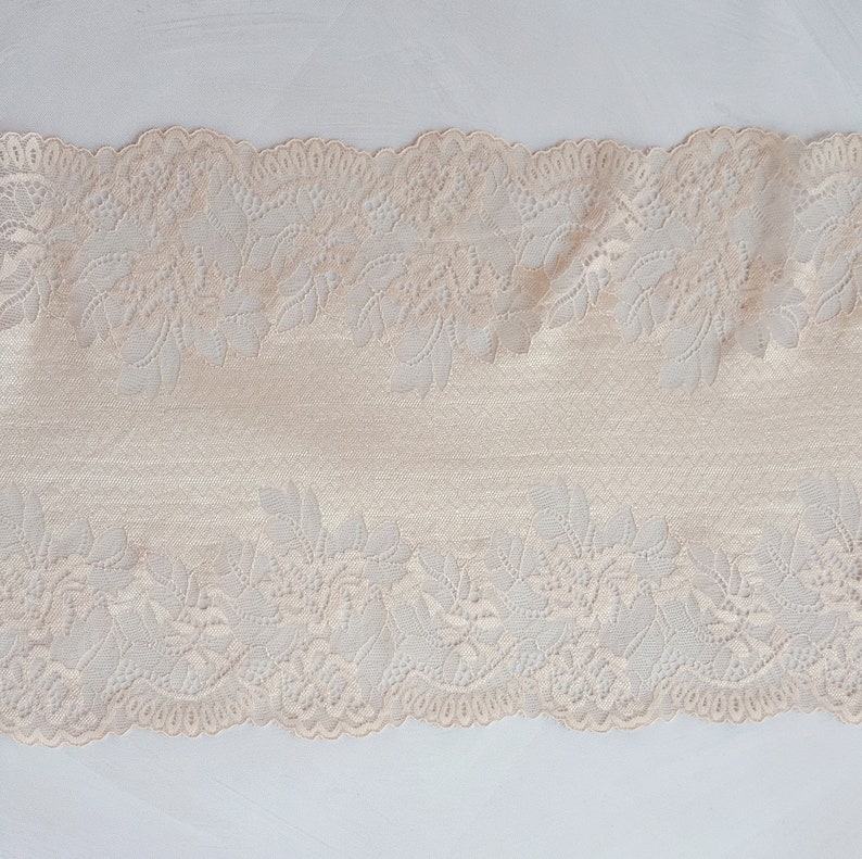 May include: Beige lace trim with a floral pattern. The lace has a scalloped edge.