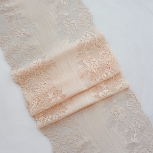 May include: Peach-colored lace trim with a delicate floral pattern. The lace is folded and has a soft, flowing texture.