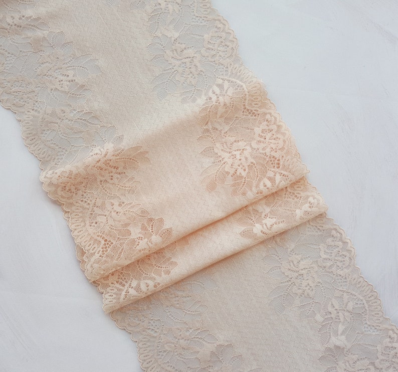 May include: Peach-colored lace trim with a delicate floral pattern. The lace is folded and has a soft, flowing texture.