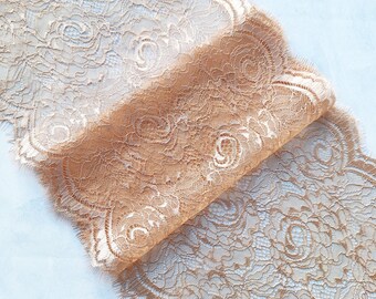 May include: A close-up of a delicate, beige lace trim with a floral pattern. The lace is soft and flowing, with a scalloped edge.